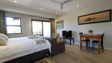 A bedroom with a bed, a sofa, a TV, a desk with chairs, and a painting on the wall.