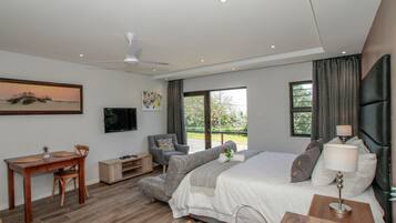 Un dormitorio moderno con cama, escritorio y silla. Hay un televisor en la pared, una ventana con cortinas y un ventilador de techo.