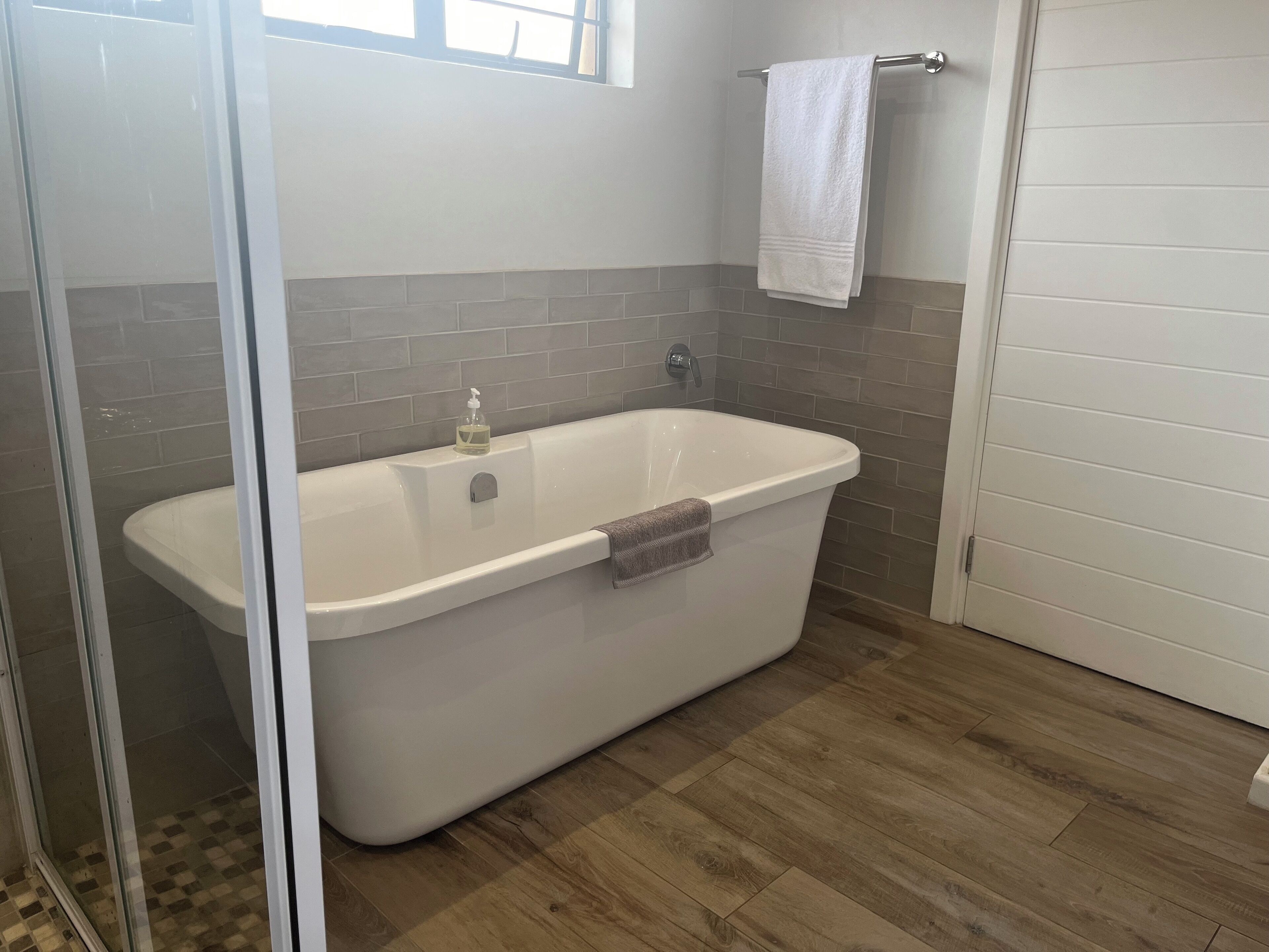 A modern bathroom with a freestanding bathtub, a glass shower enclosure, and a wooden floor.