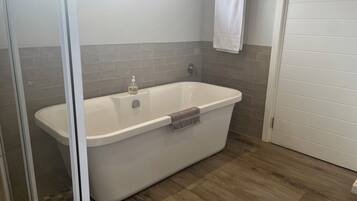A modern bathroom with a freestanding bathtub, a glass shower enclosure, and a wooden floor.