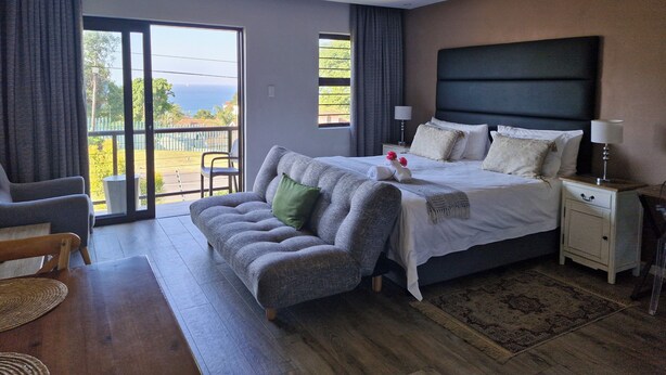 A modern bedroom with a large bed, a sofa, a small table, and a ceiling fan. - Casa Ridge (Umhlanga)