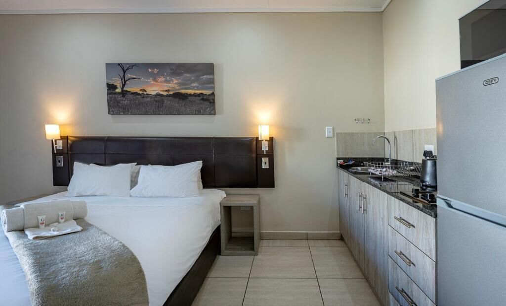 Een hotelkamer met een bed, nachtkastje, lamp en uitzicht op het keukenruimte.
