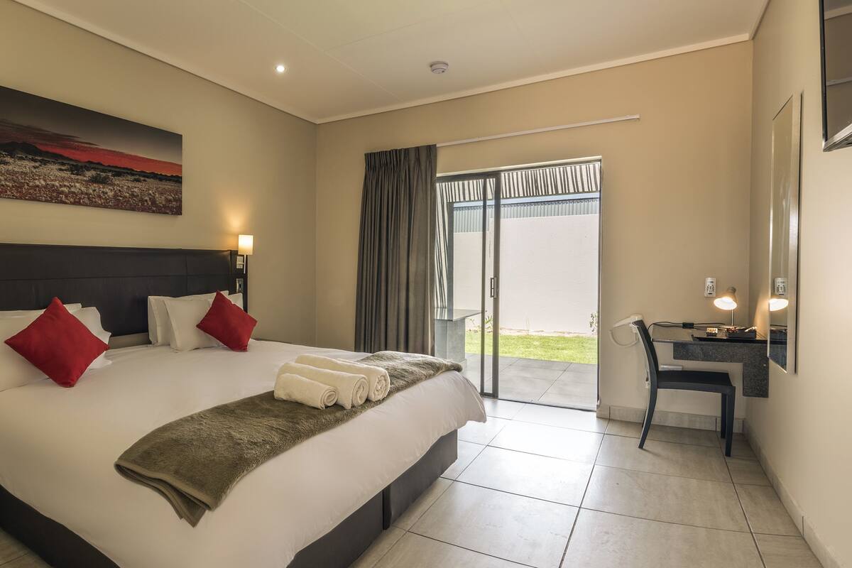 A hotel room with a large bed, a desk, a chair, and a balcony with a view.
