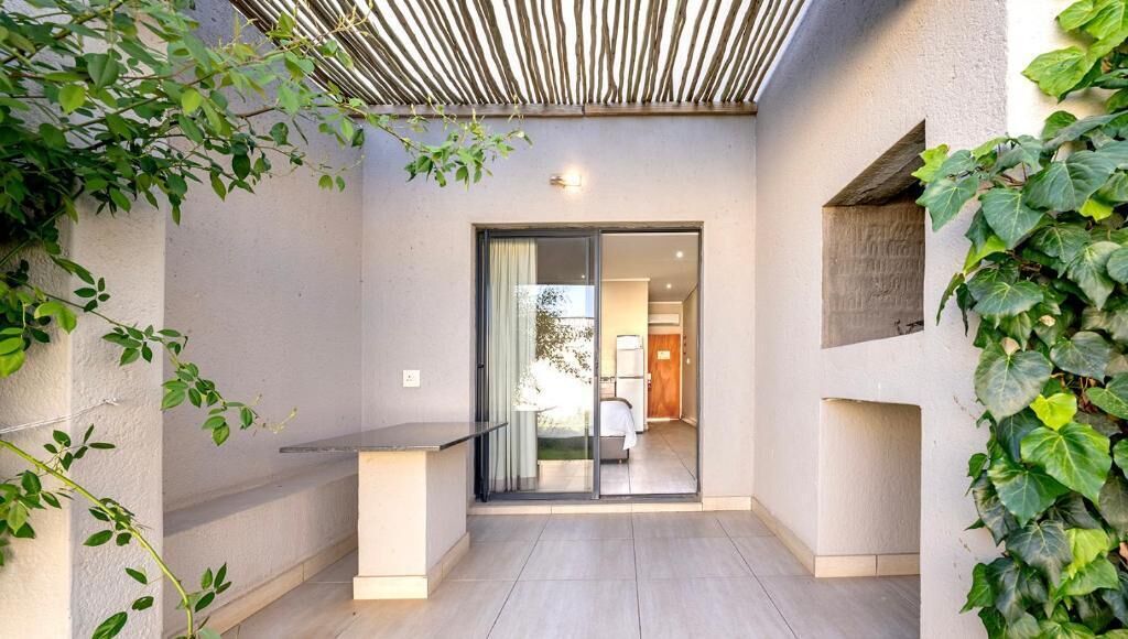 Área externa moderna com porta de vidro que dá para um espaço interno, rodeada por vegetação.