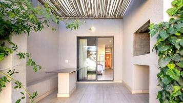 Área externa moderna com porta de vidro que dá para um espaço interno, rodeada por vegetação.