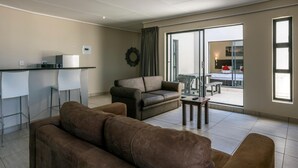 A modern living room with a sofa, a coffee table, and a dining area with a bar. - Pofadder Inn by Country Hotels (Khâi-Ma)