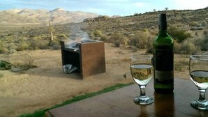 Paisaje desértico con una parrilla y una botella de vino sobre una mesa.