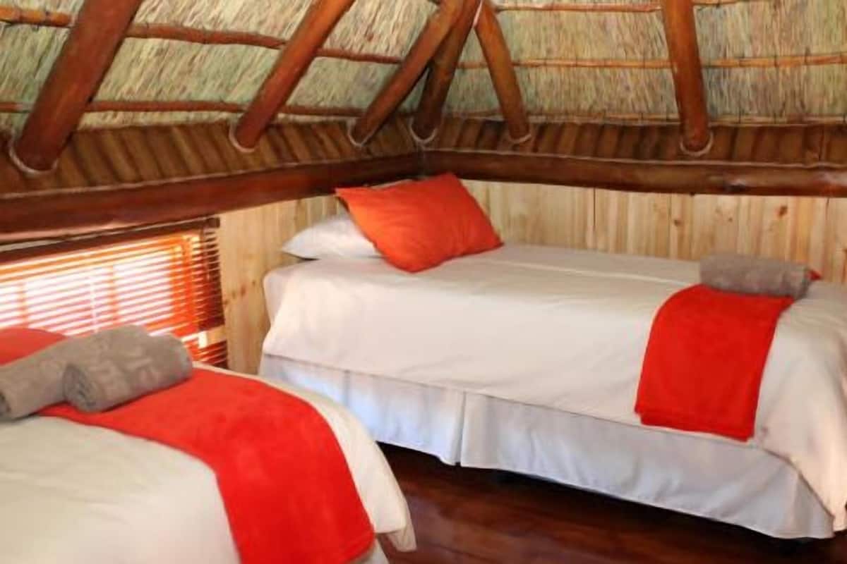 Een kamer met twee bedden, elk voorzien van witte beddengoed en rode accenten, houten balken in het plafond en een raam met luiken.