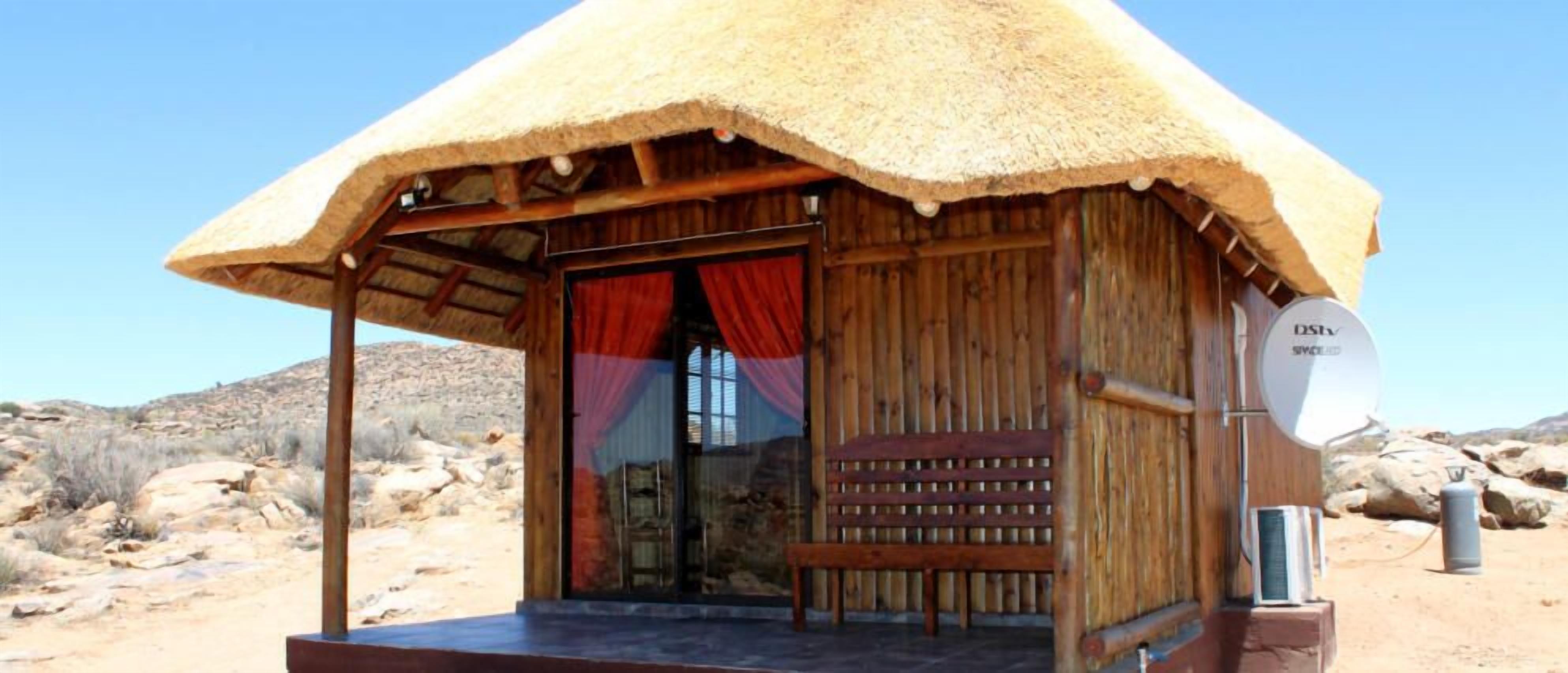 A wooden hut with a thatched roof, a bench outside, and a satellite dish on the right.
