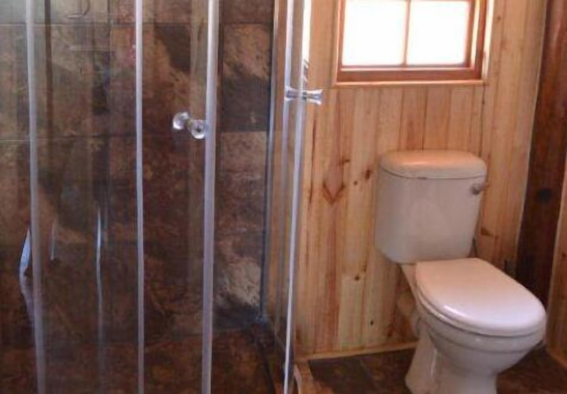 Un baño con pared de madera, cabina de ducha de vidrio y un inodoro.