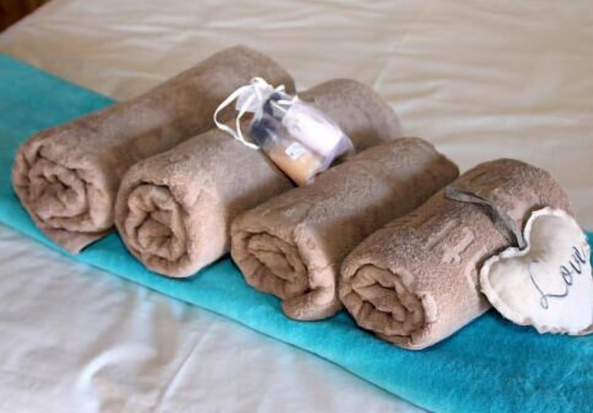 A bed with rolled towels and a small bottle of lotion.