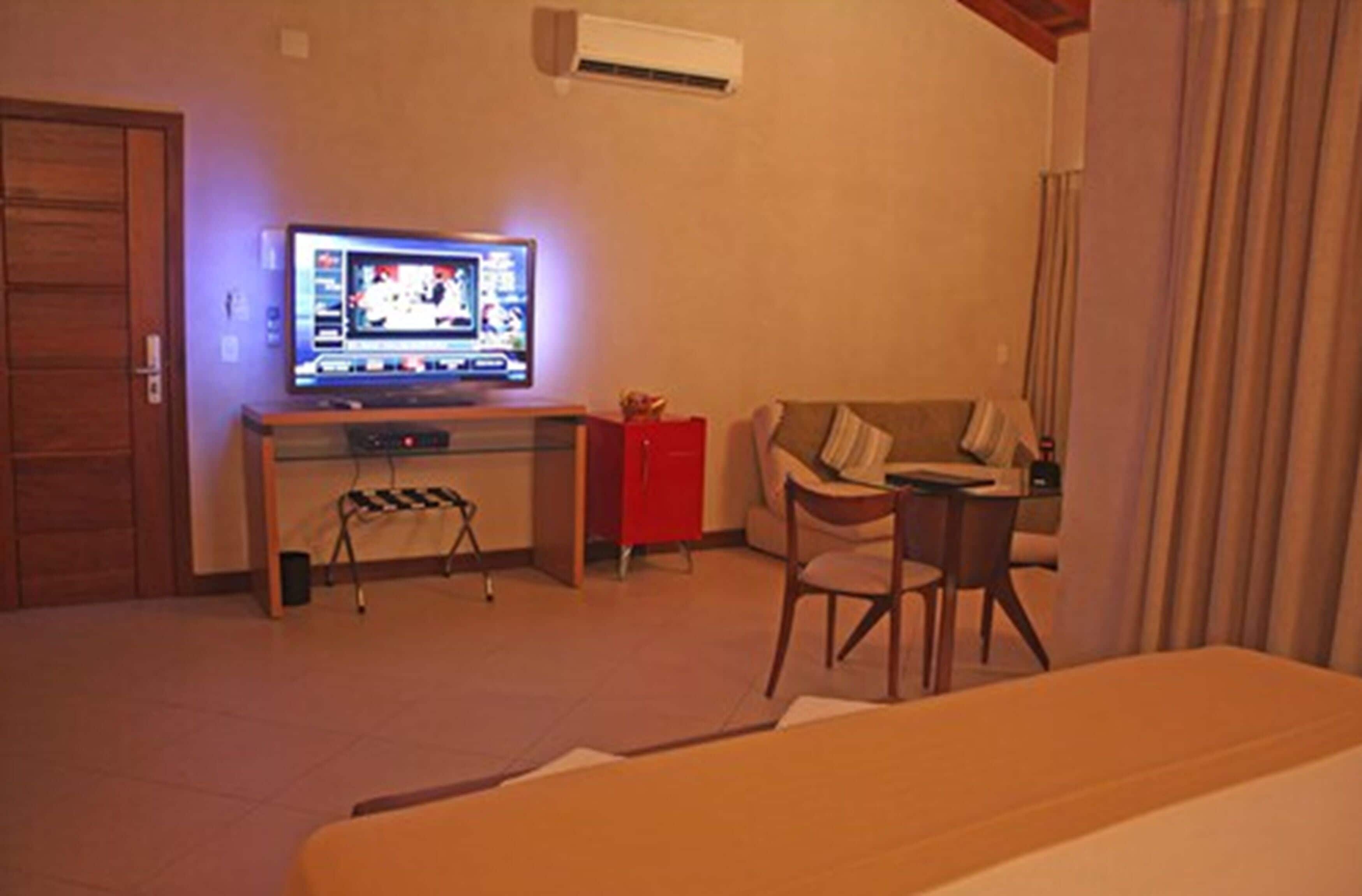 A hotel room with a bed, a desk with a computer, a TV, a chair, and a small table.