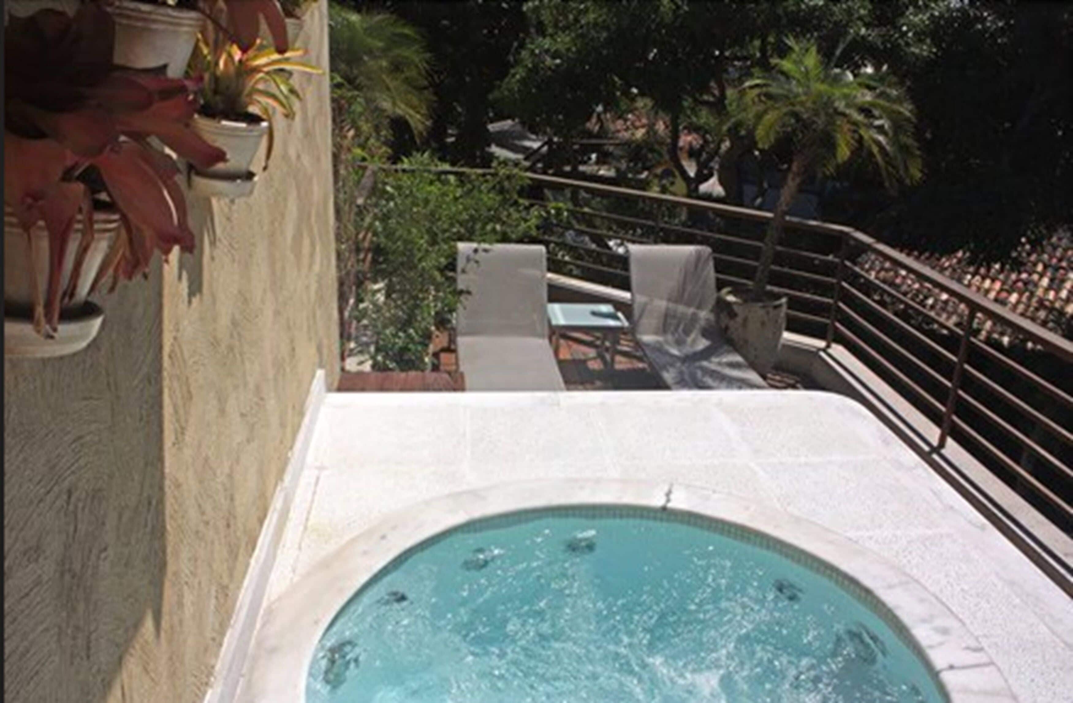 A pool area with a hot tub, lounge chairs, and a railing overlooking a crowd.