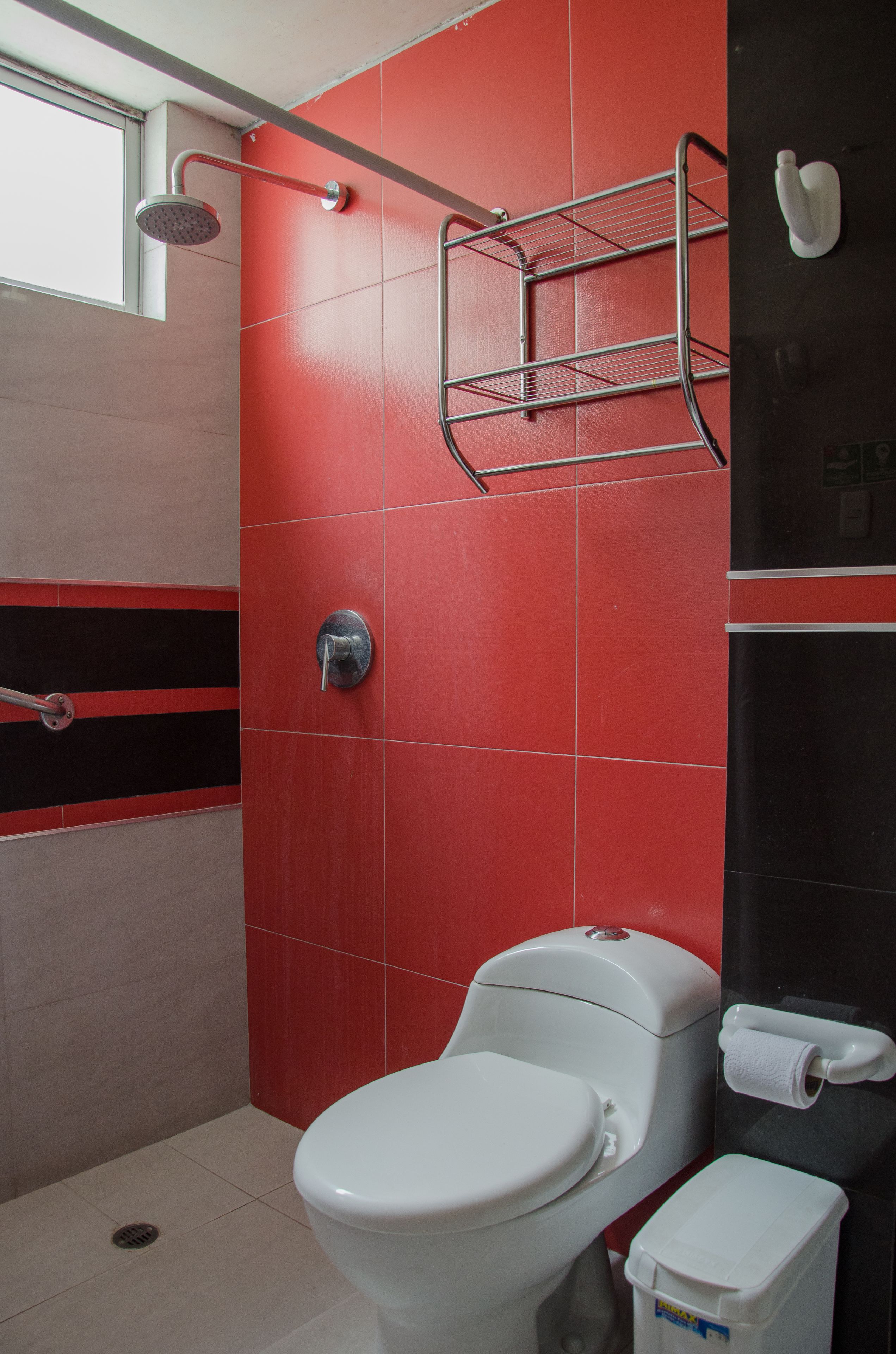 Un baño con inodoro blanco, ducha y pared con azulejos negros y rojos.