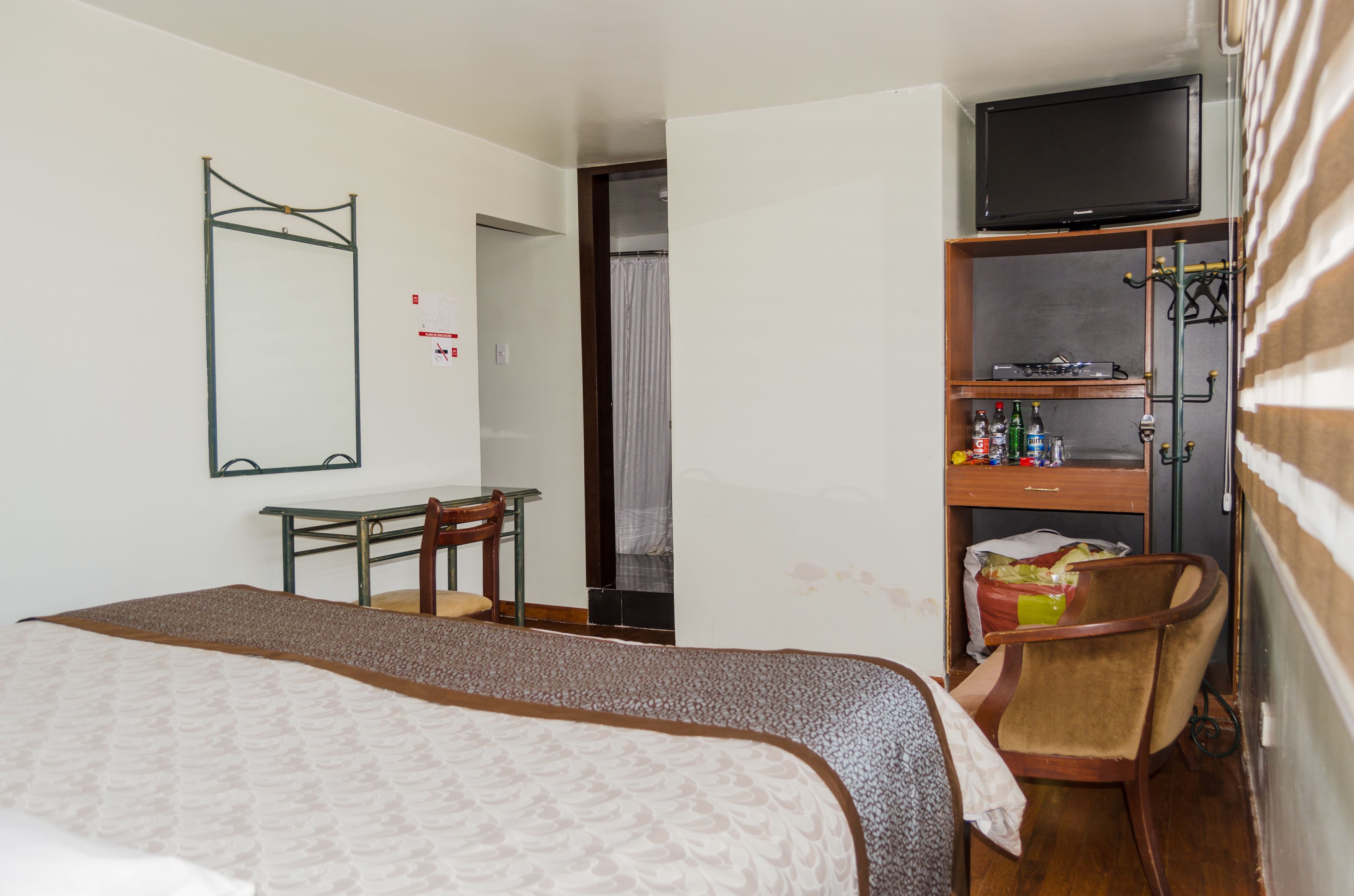 A hotel room with a bed, a desk, a chair, a television, and a minibar.