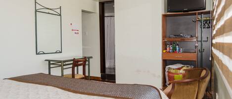 A hotel room with a bed, a desk, a chair, a television, and a minibar.