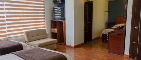 Habitación de hotel con dos camas, un televisor, un armario de madera y una puerta que da a otra habitación.