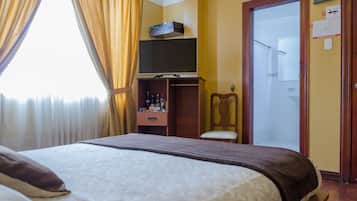 Hotelkamer met een bed, een televisie op een standaard, een houten kledingkast, een stoel en een deur naar een badkamer.