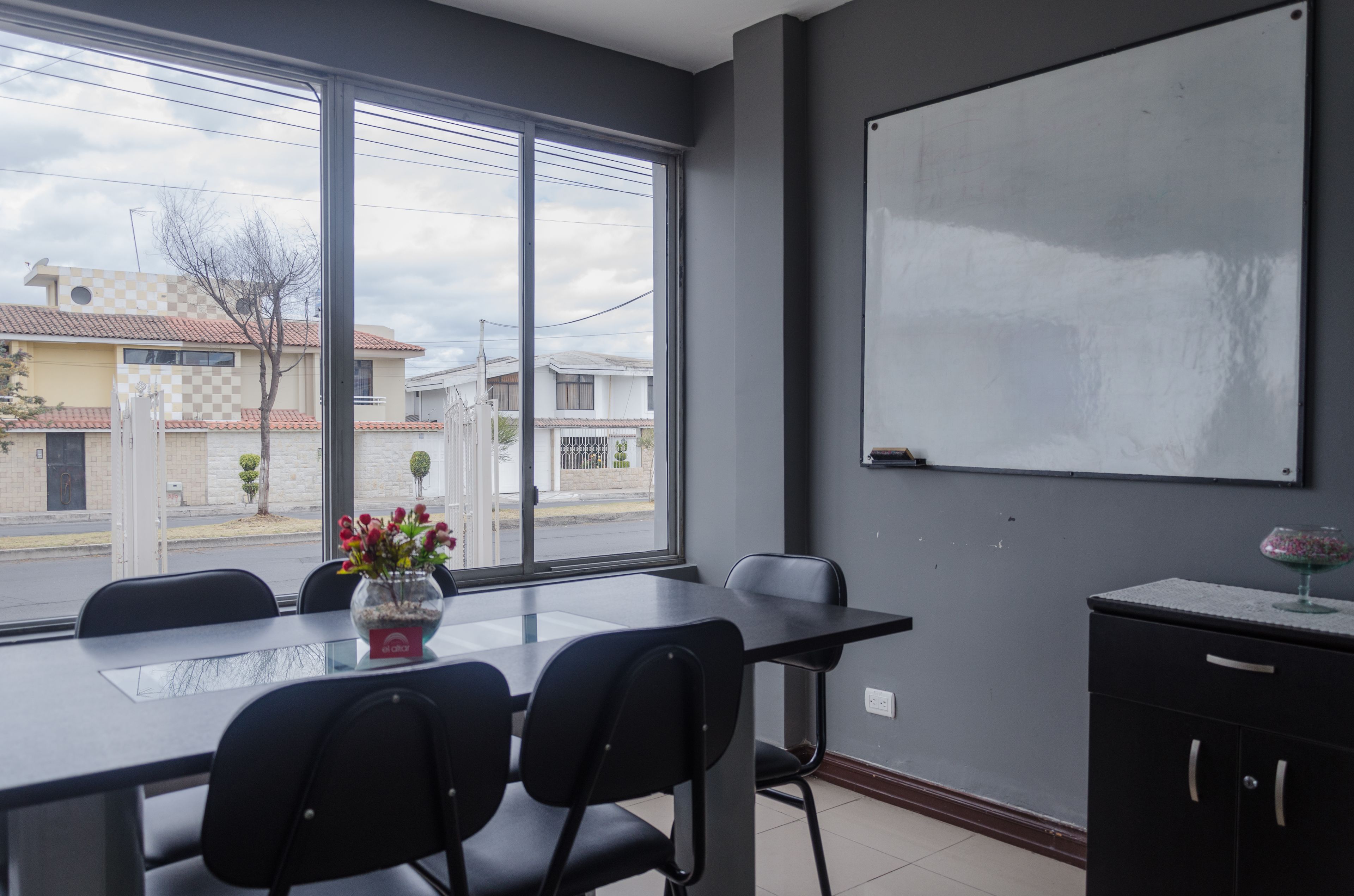 A conference room with a large window, a whiteboard, and a table with chairs.