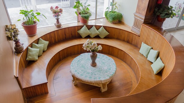A curved wooden bench seating area with a central round table, surrounded by potted plants and cushions. - Hotel El Altar (Riobamba)