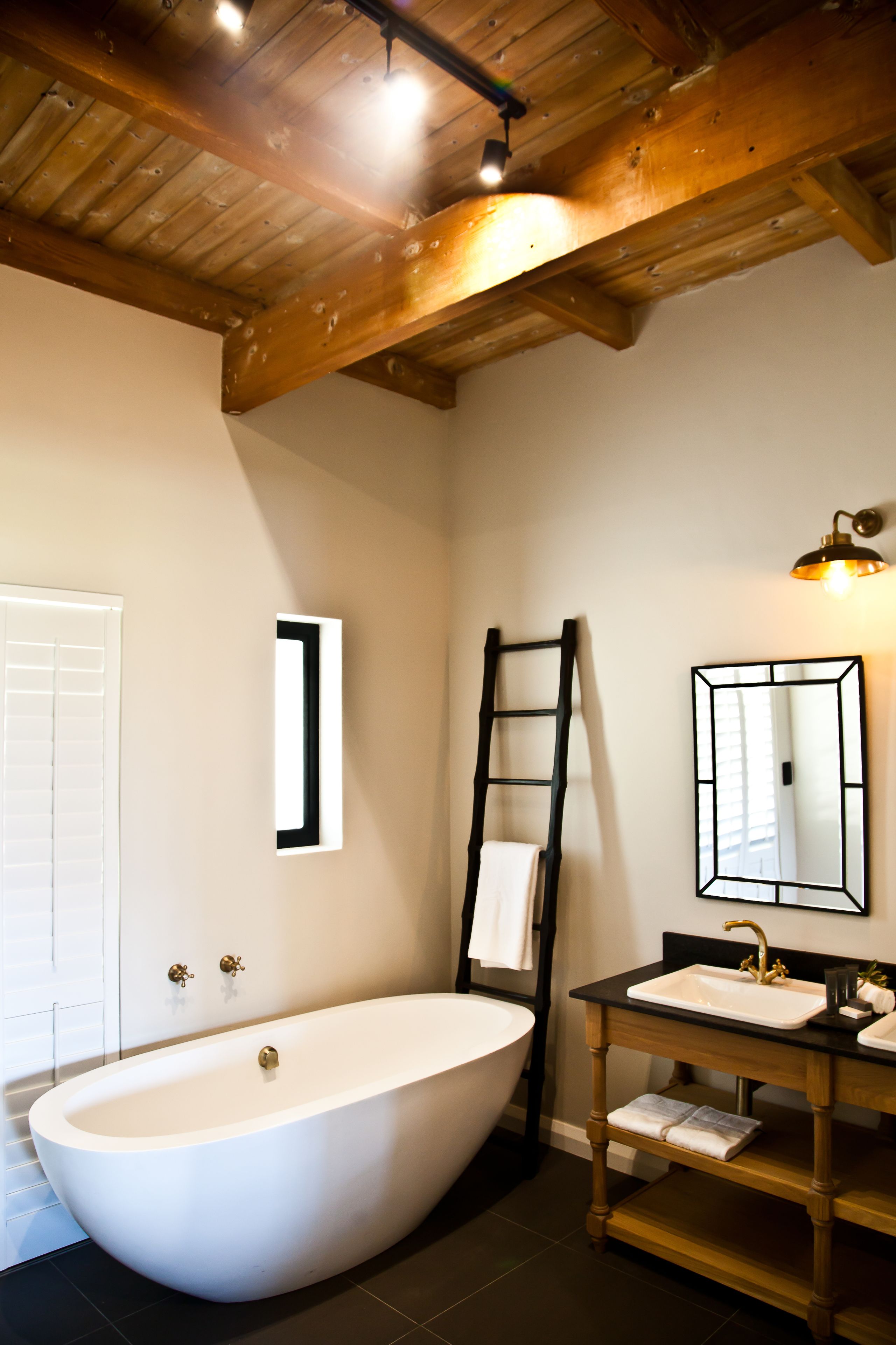 A bathroom with a freestanding bathtub, a wooden vanity with a mirror, and a ladder leaning against the wall.