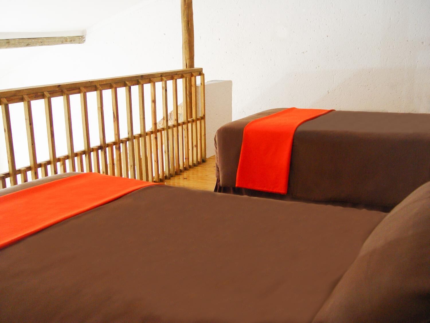 A room with two beds, each covered with brown sheets and orange blankets.