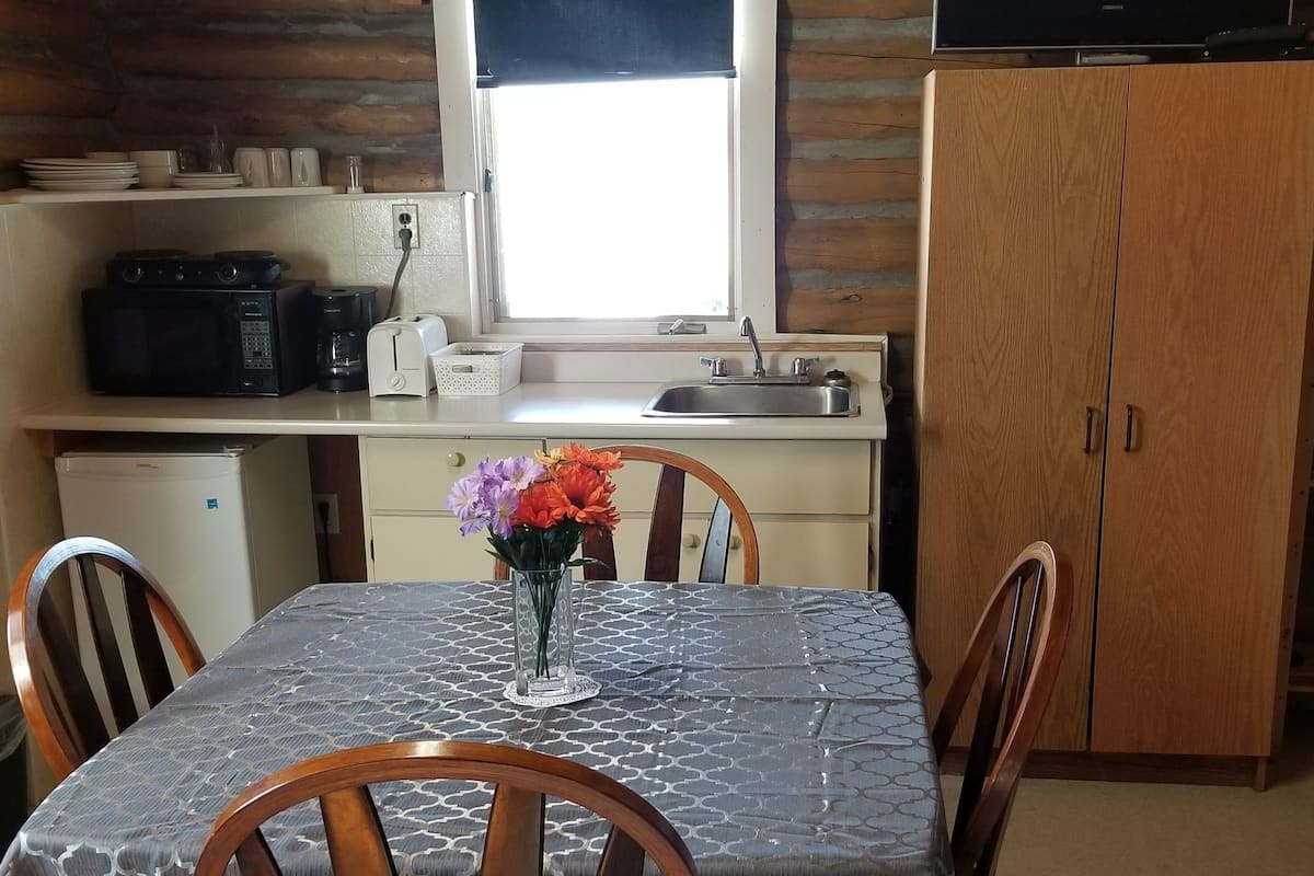 A cozy cabin-style kitchen with a dining table, chairs, a microwave, toaster, and a television.