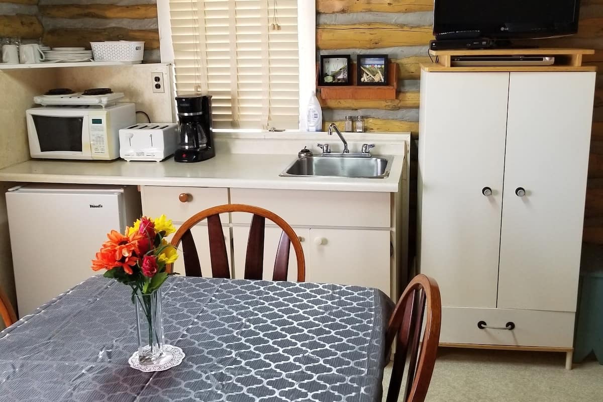 A cozy kitchen with wooden walls, a dining table with a patterned tablecloth, and a TV on a wooden stand.