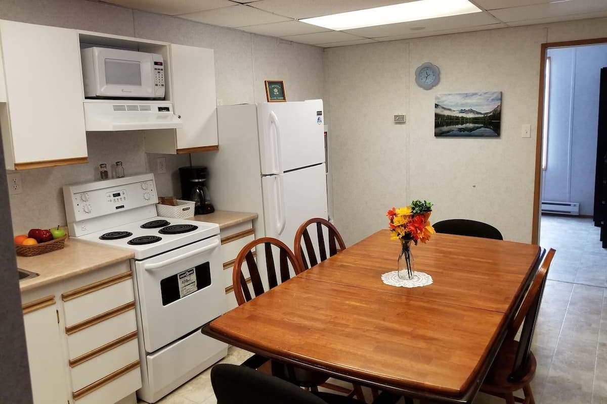 A compact kitchen with a microwave, stove, refrigerator, and a dining table with chairs.