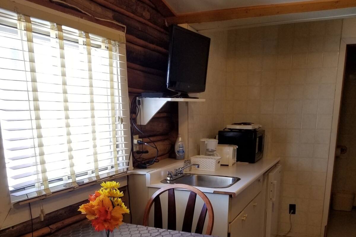 A compact kitchen with a built-in microwave, a sink, and a flat-screen TV mounted above it.