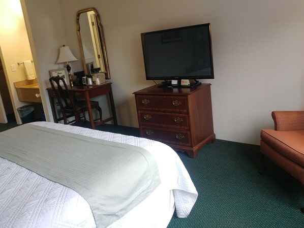 Une chambre d’hôtel avec un lit, un téléviseur posé sur une commode en bois, une chaise et un bureau avec une lampe.