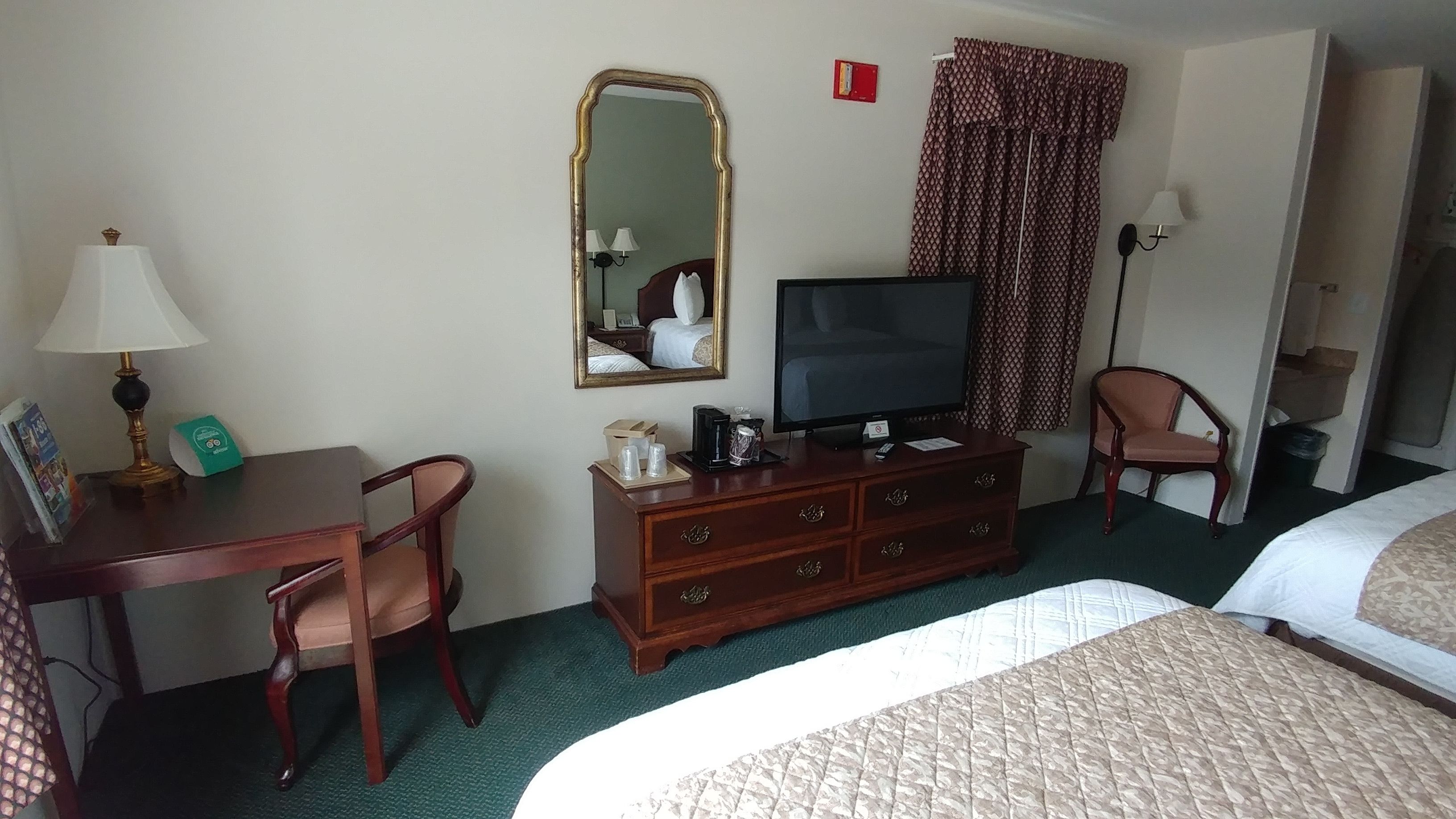 Een hotelkamer met een bed, een bureau met lamp, een televisie, een kaptafel en een stoel.