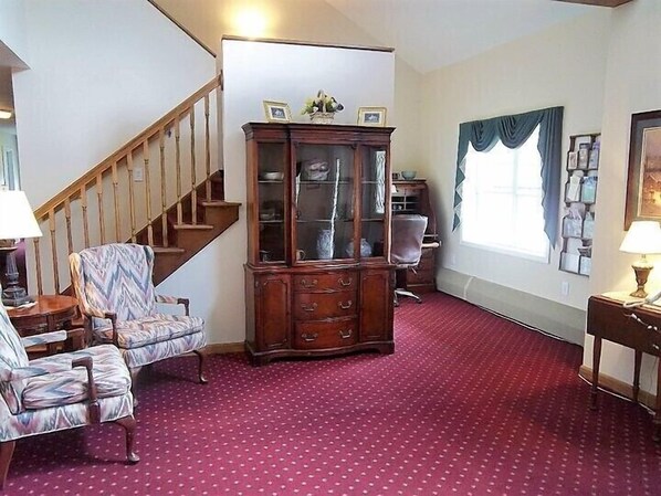 Una sala de estar con escalera, un aparador de madera, sillas estampadas y una alfombra roja.