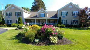 A two-story house with a front porch, a well-maintained lawn, and a flower bed with various flowers. - The Inn At Houghton Creek (Houghton)