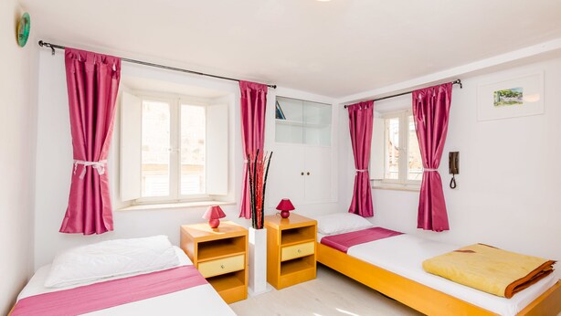 Una habitación con dos camas, una mesita de noche de madera, un espejo y cortinas rosadas.