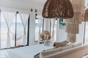 Quarto à beira-mar com cama, janelas amplas e uma cadeira de vime.