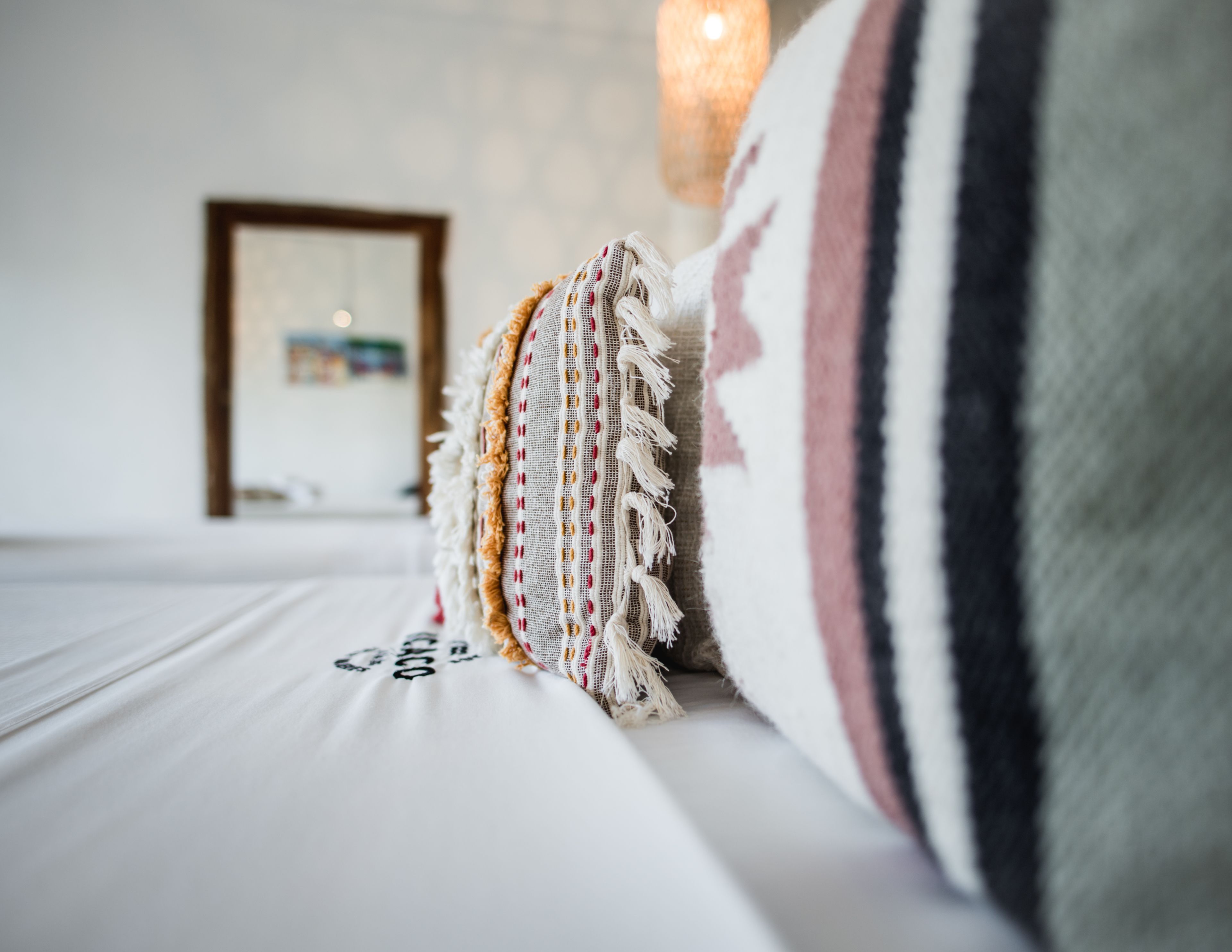 Una cama con sábana blanca y almohada decorativa con flecos.
