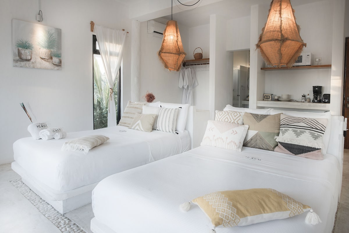 A hotel room with two beds, a large window with curtains, a hanging basket, and a shelf with a coffee maker.