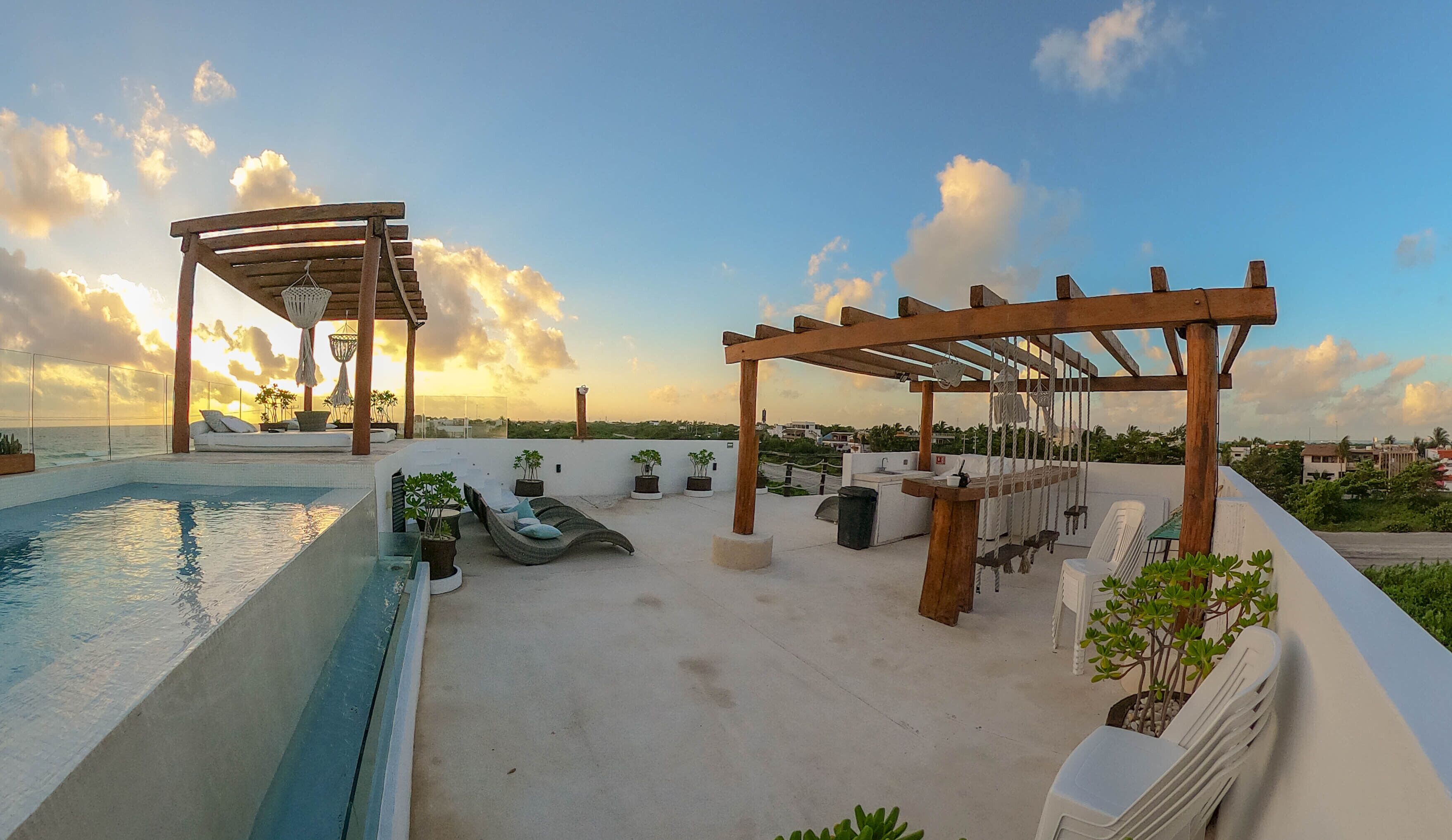 A rooftop pool area with a pergola, lounge chairs, and potted plants.