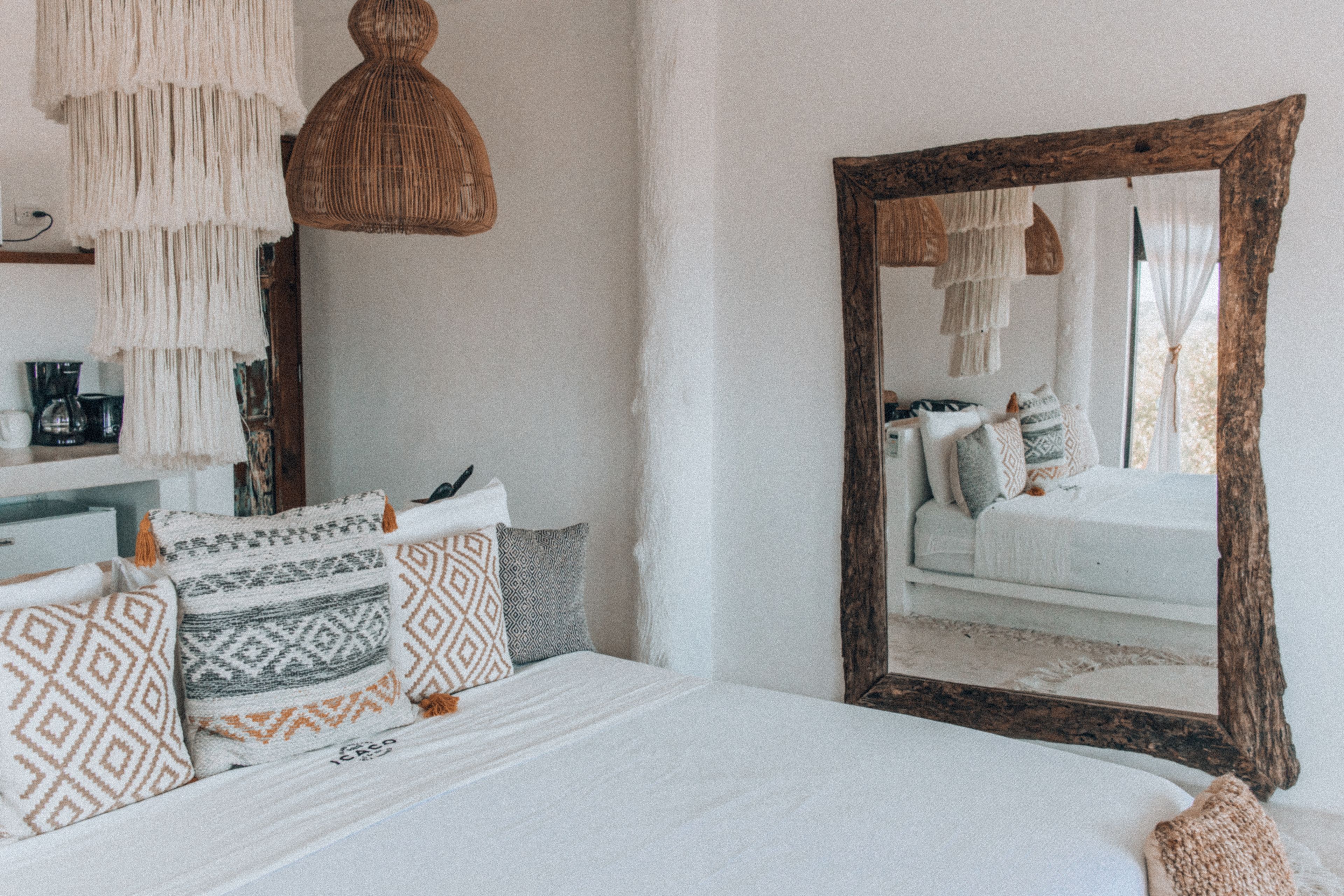 Un dormitorio con un espejo grande, almohadas estampadas y una lámpara colgante.