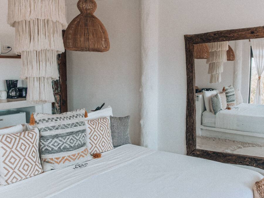Un dormitorio con un espejo grande, almohadas estampadas y una lámpara colgante.