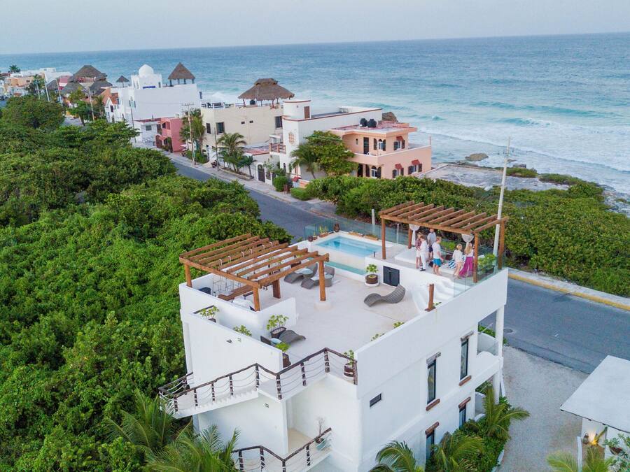Un resort costero con piscina en la azotea, abundante vegetación y vistas al océano.