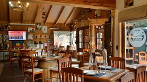 A rustic wooden interior with wooden tables and chairs, a bar area, and a television displaying a menu. - Hotel Borde Andino (Pinto)
