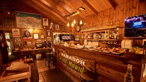 A bar with wooden decor, a clock, and a TV screen displaying a cityscape. - Hotel Borde Andino (Pinto)