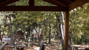 A wooden deck leading into a forested area with a cabin in the background. - Hotel Borde Andino (Pinto)