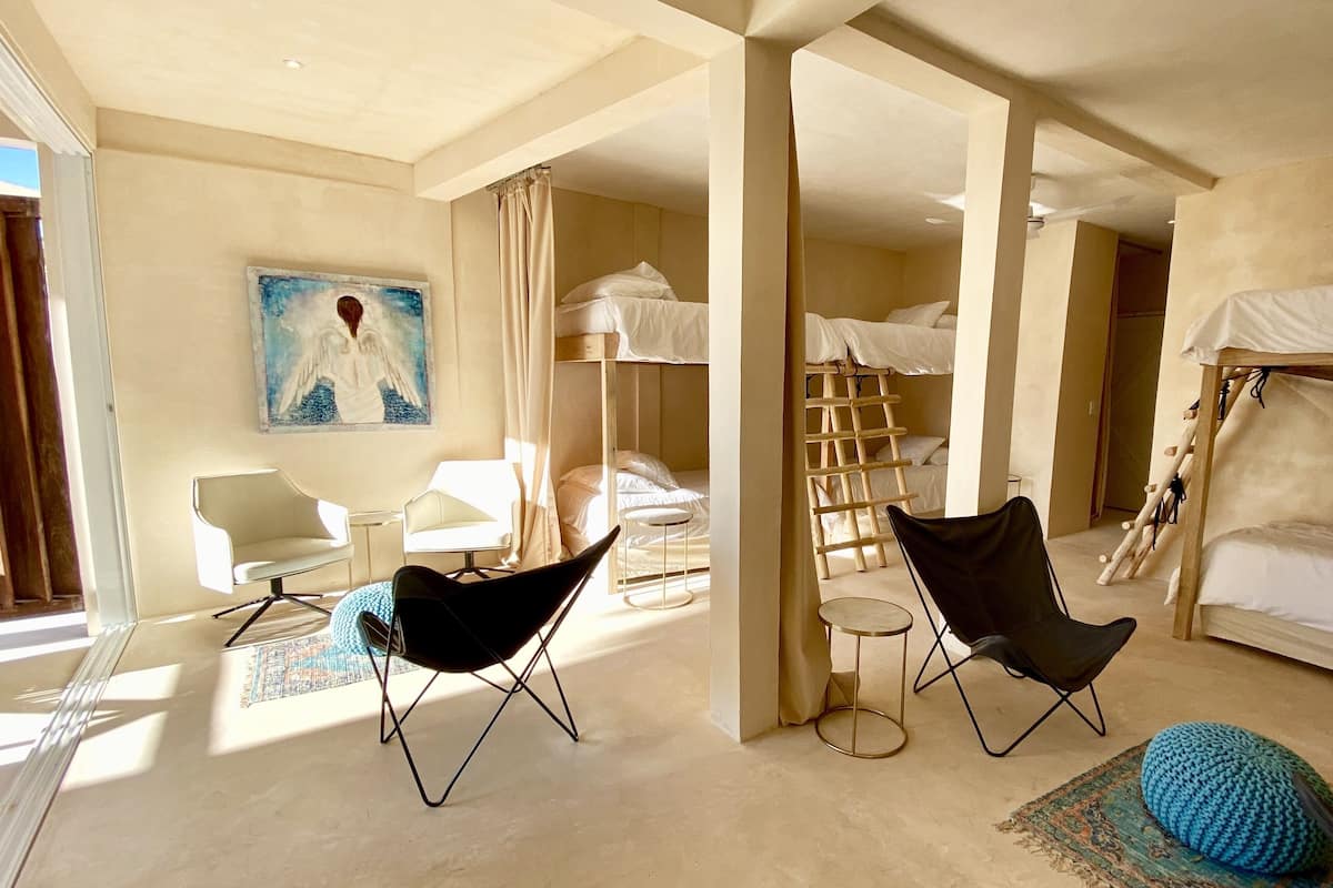A modern hotel room with bunk beds, a painting, a desk, and two chairs.