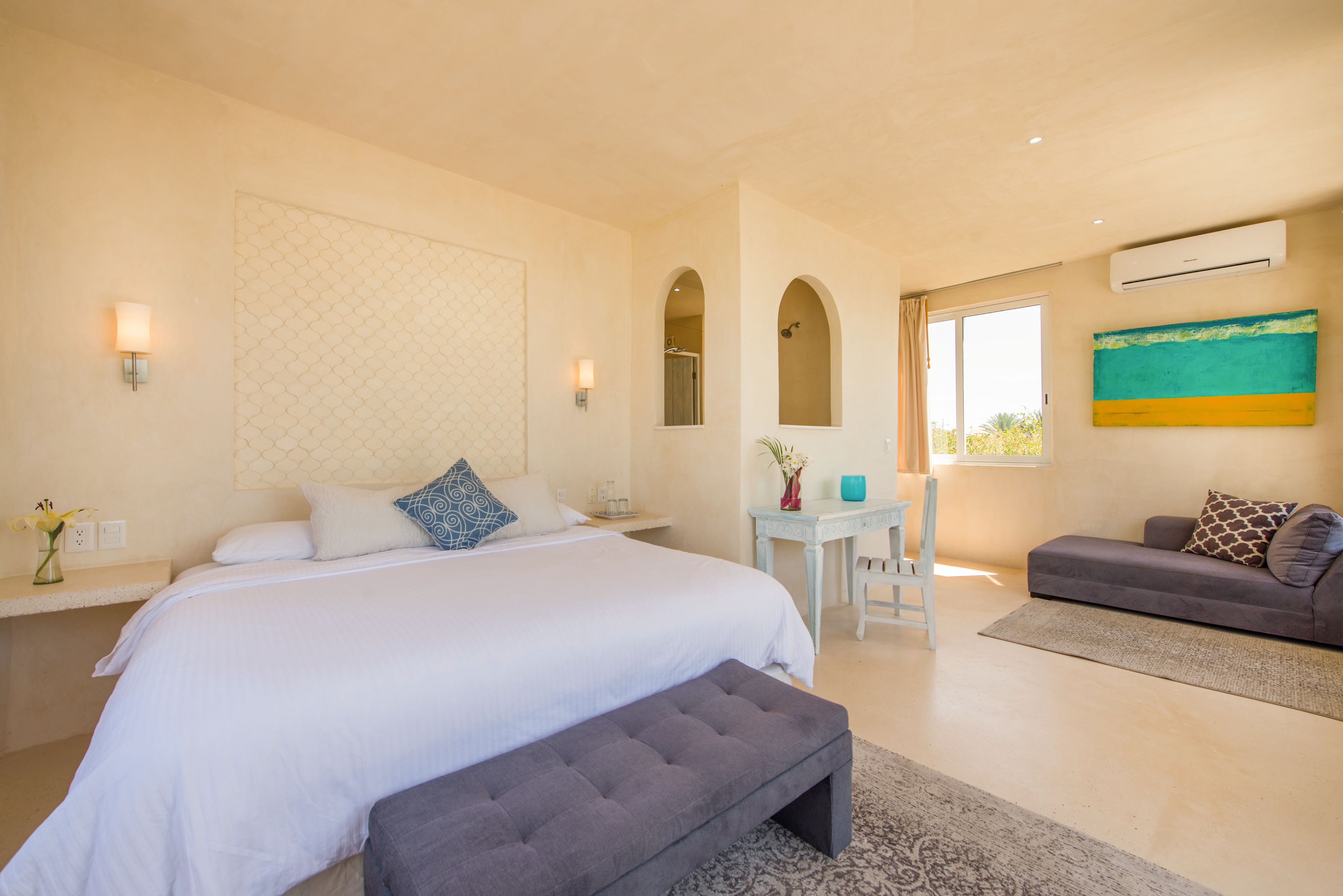 A bedroom with a large bed, a desk, a sofa, and an arched window.