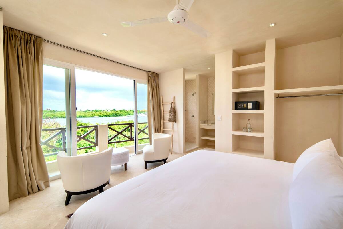A spacious bedroom with a large bed, a sitting area with a chair, and a wardrobe.
