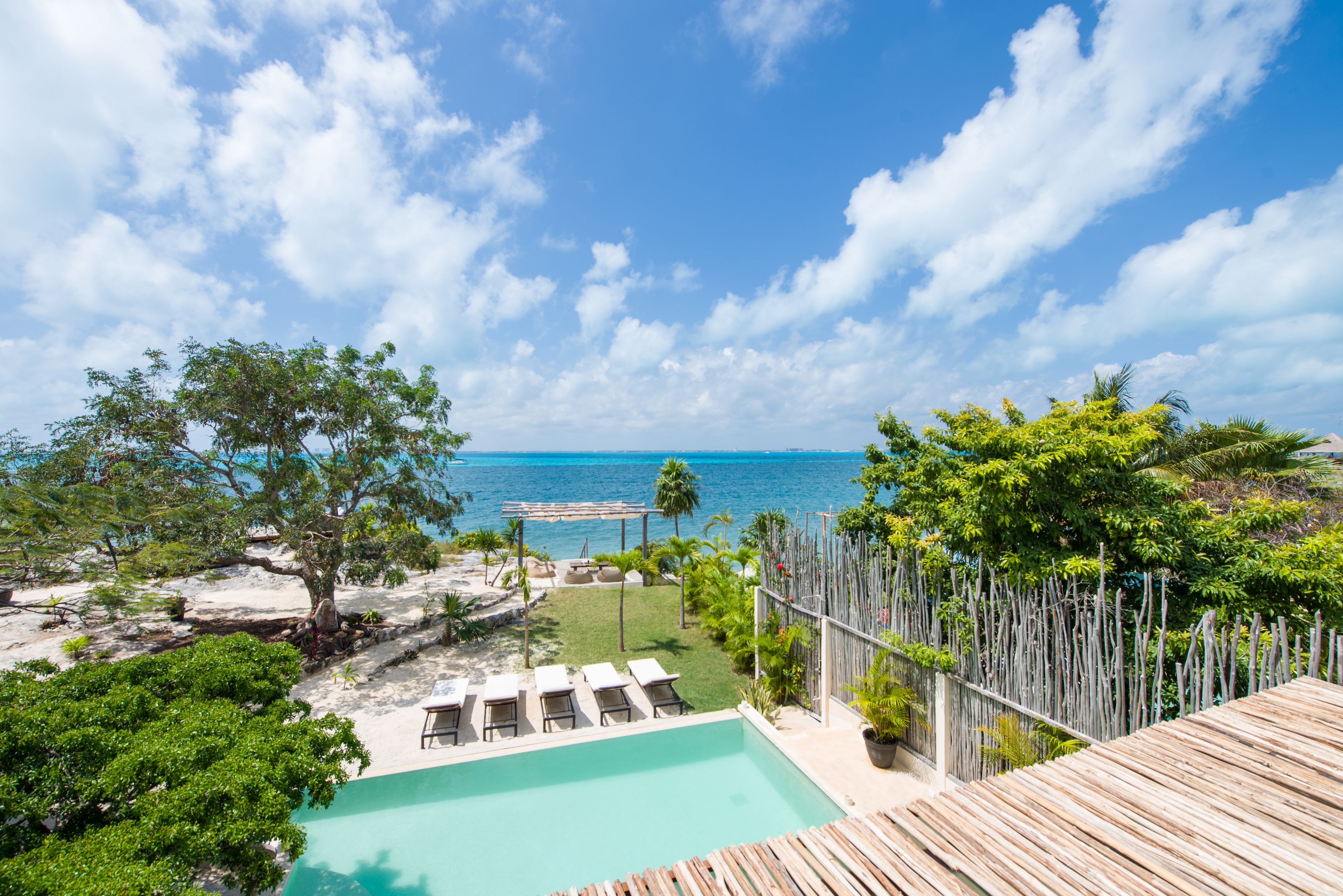 A pool area with lounge chairs, a wooden deck, and a view of the ocean.