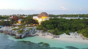 Una propiedad frente a la playa con un edificio de techo de paja, una playa de arena y aguas turquesas cristalinas.